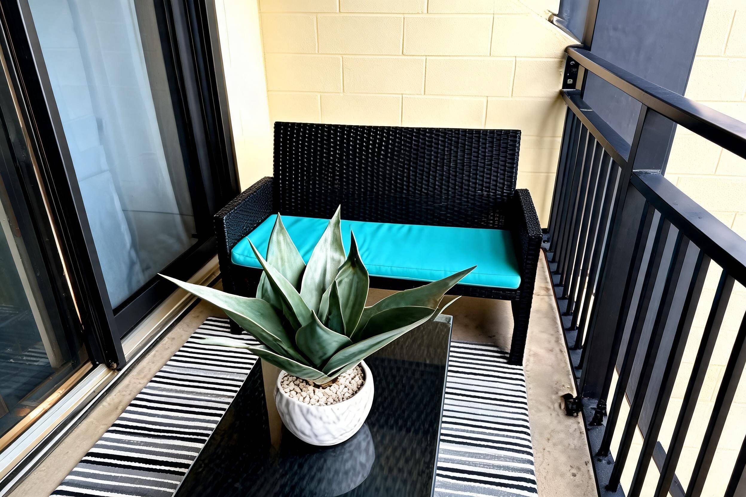A balcony with a black wicker sofa, a potted plant, and a striped rug.