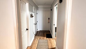 Un pasillo con puertas blancas, suelo de madera y felpudo negro.