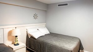 Un dormitorio con una cama, una mesita de noche, una lámpara, un reloj de pared y una rejilla de ventilación.