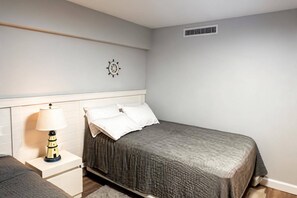 Ein Schlafzimmer mit einem Bett, einem Nachttisch, einer Lampe, einer Wanduhr und einem Lüftungsgitter.