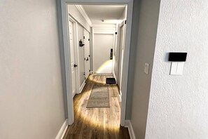 Un pasillo con paredes blancas, suelo de madera y una puerta al final.