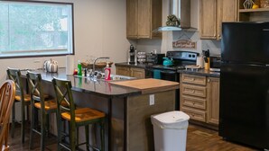 Une cuisine moderne avec des meubles en bois, un réfrigérateur noir, un îlot central doté de tabourets de bar et une fenêtre avec des stores.