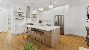 Una cocina moderna con una isla grande, taburetes de bar, luces colgantes y electrodomésticos de acero inoxidable.