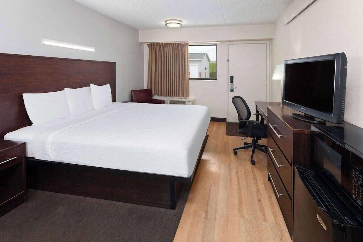 A hotel room with a large bed, a desk with a television, a chair, and a minibar.