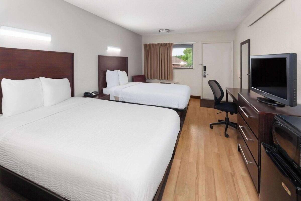 A hotel room with two beds, a desk with a TV, and a window with curtains.