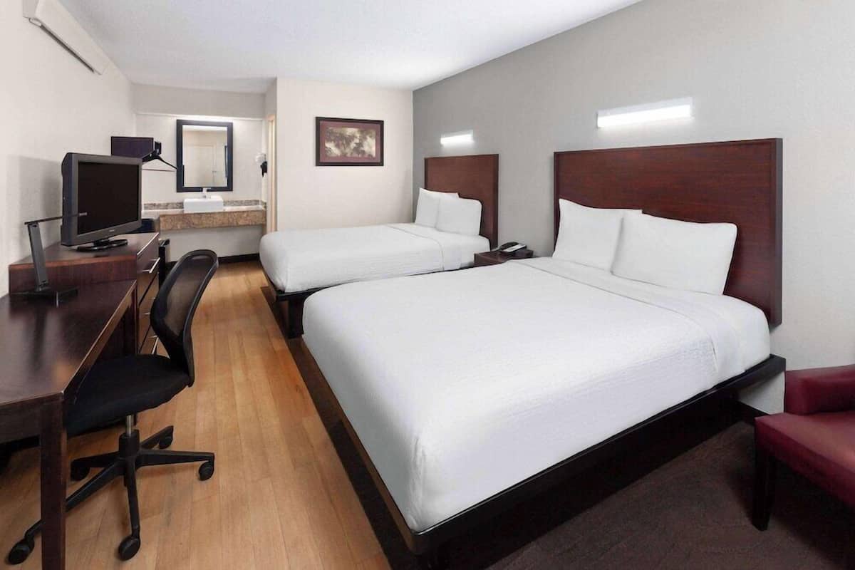 A hotel room with two single beds, a desk with a computer, a chair, and a TV.