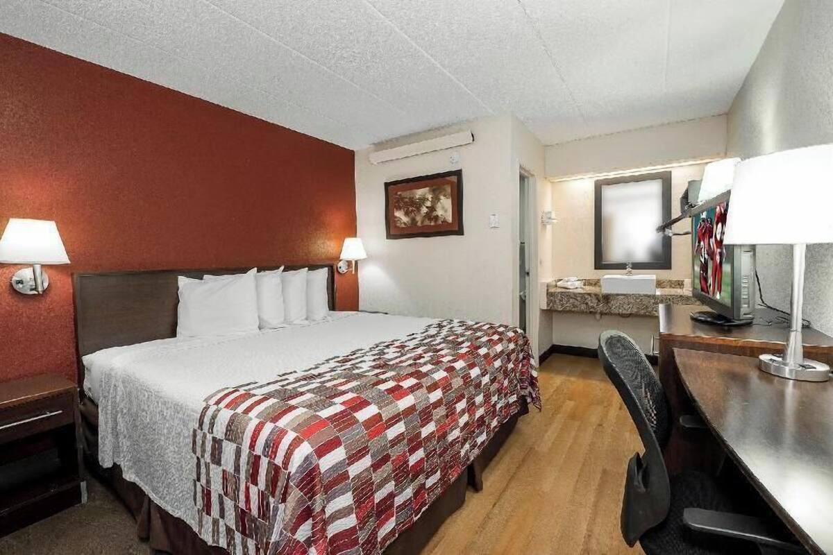 A hotel room with a bed, two bedside lamps, a desk with a computer, a chair, and a television.