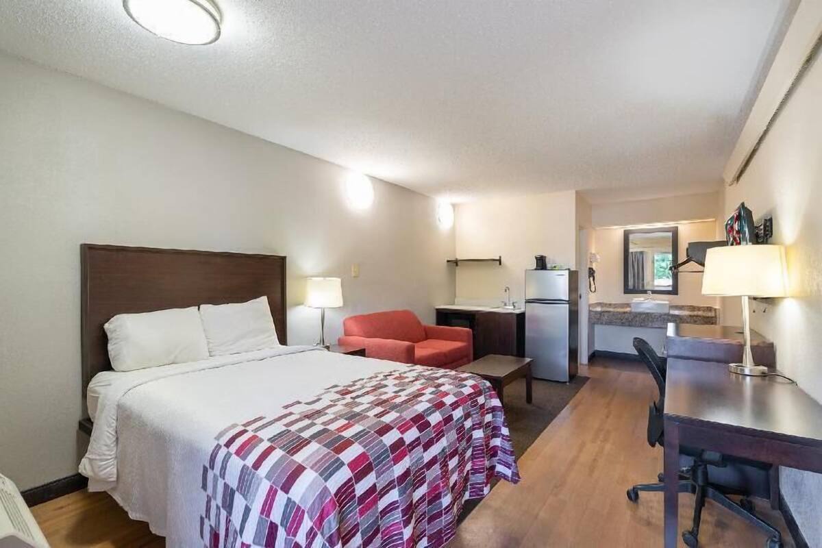 A hotel room with a bed, a desk, a chair, a kitchenette, and a bathroom.