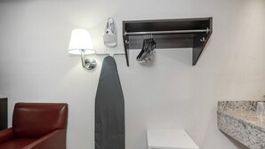 Un baño con toallero, tabla de planchar en la pared, una silla y panel de control.