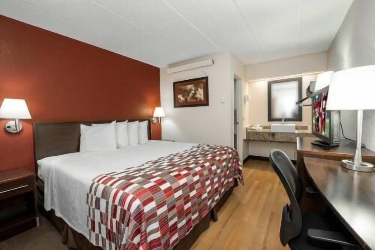 A hotel room with a bed, bedside lamps, a desk with a chair, and a television.