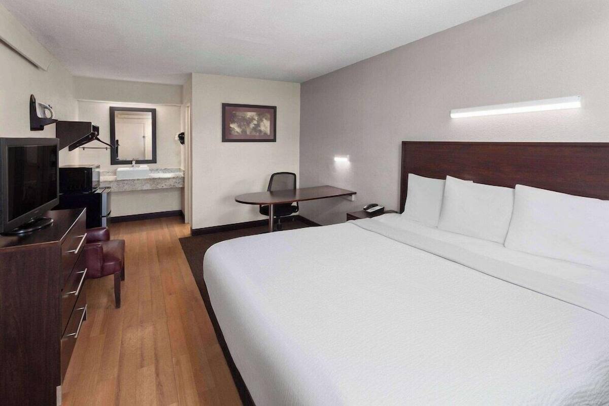 A hotel room with a large bed, a desk, a chair, a television, a mirror, and a picture on the wall.