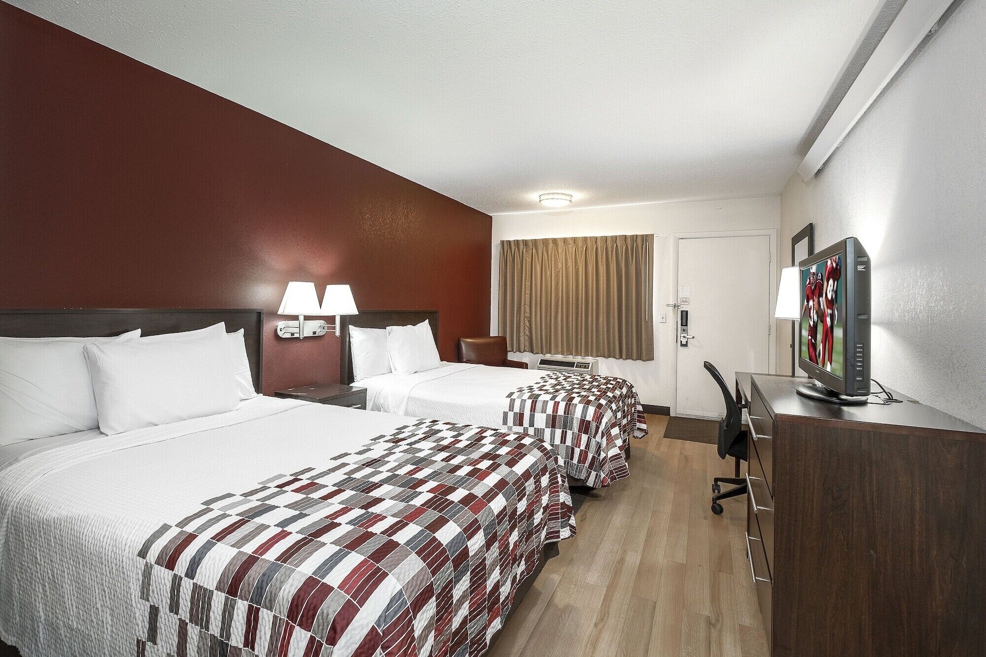 A hotel room with two beds, a desk with a television, and a chair.