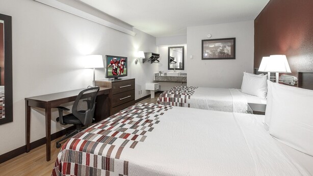Habitación de hotel con cama, escritorio, silla, televisor, baño y un cuadro en la pared.