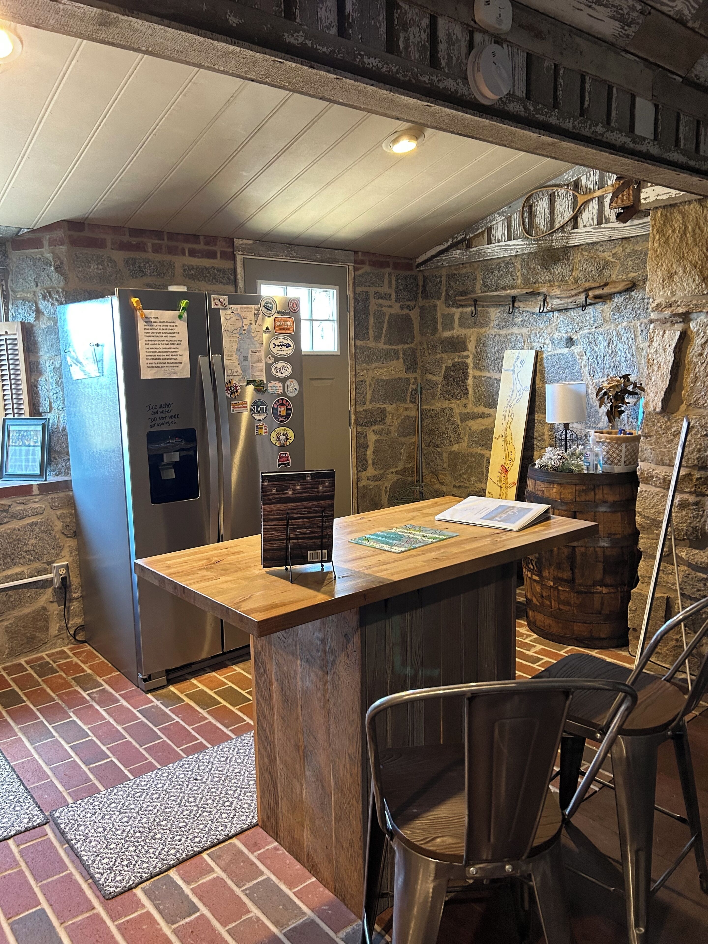 Une cuisine avec un îlot central en bois, des murs en pierre, un réfrigérateur décoré d’aimants et un décor rustique.