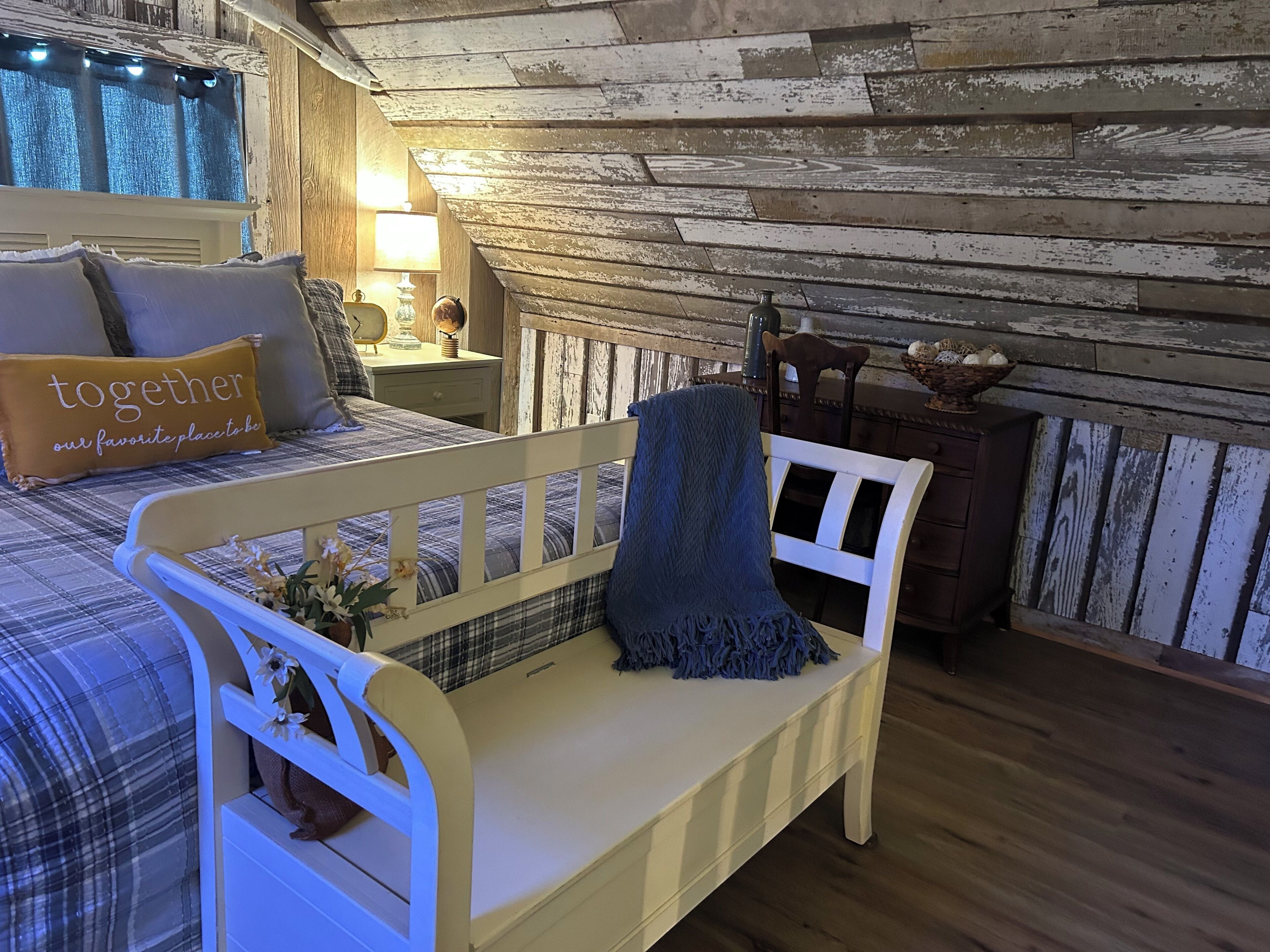 Ein gemütliches Schlafzimmer mit Bett, Sitzbank, Nachttisch und Lampe.