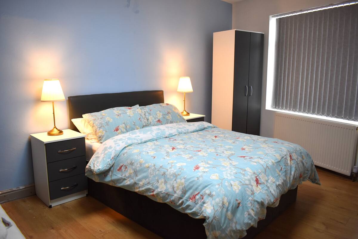 A bedroom with a bed, two bedside tables with lamps, a wardrobe, and a window with blinds.