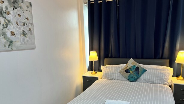 A neatly made bed with striped bedding, a folded towel, and a decorative pillow. There are two bedside lamps on nightstands, and a dark curtain covers the window. - Pleasant Apartment in City Center (Birmingham)