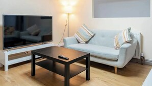 A modern living room with a flat-screen TV, a light grey sofa, a wooden coffee table, and a floor lamp. - Pleasant Apartment in City Center (Birmingham)