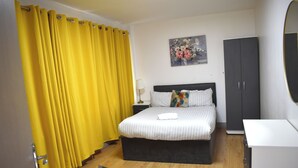 A bedroom with a bed, a wardrobe, a painting, and a yellow curtain. - Pleasant Apartment in City Center (Birmingham)
