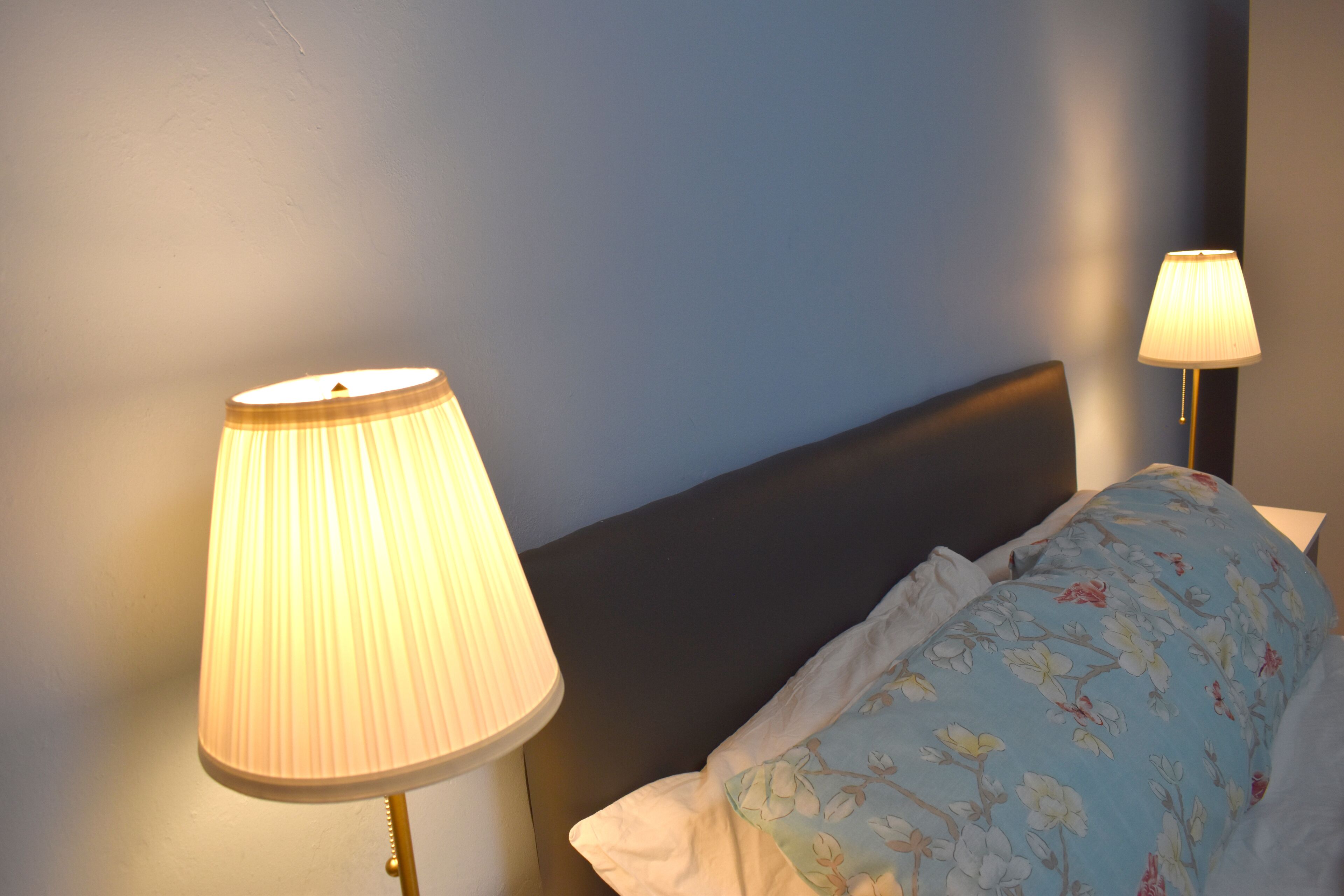 A bedroom with a bed, two bedside lamps, and a floral pillow.