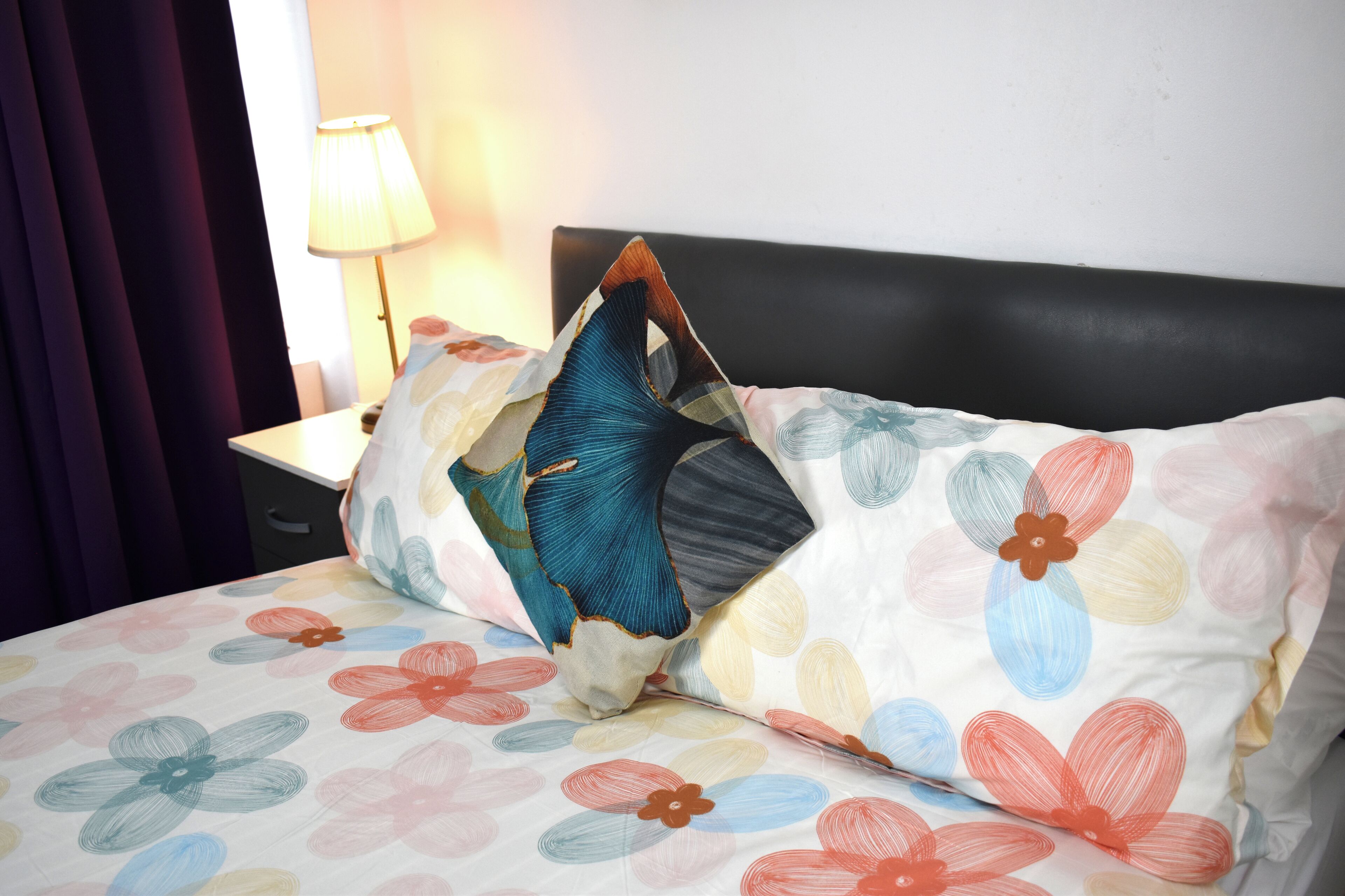 Un lit avec une couvre-lit à motifs floraux et un oreiller aux couleurs bleu et orange.
