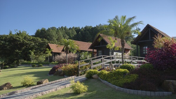 A traditional wooden house with a thatched roof, surrounded by lush greenery and a well-maintained lawn. - Pousada Scursel (Ibirama)
