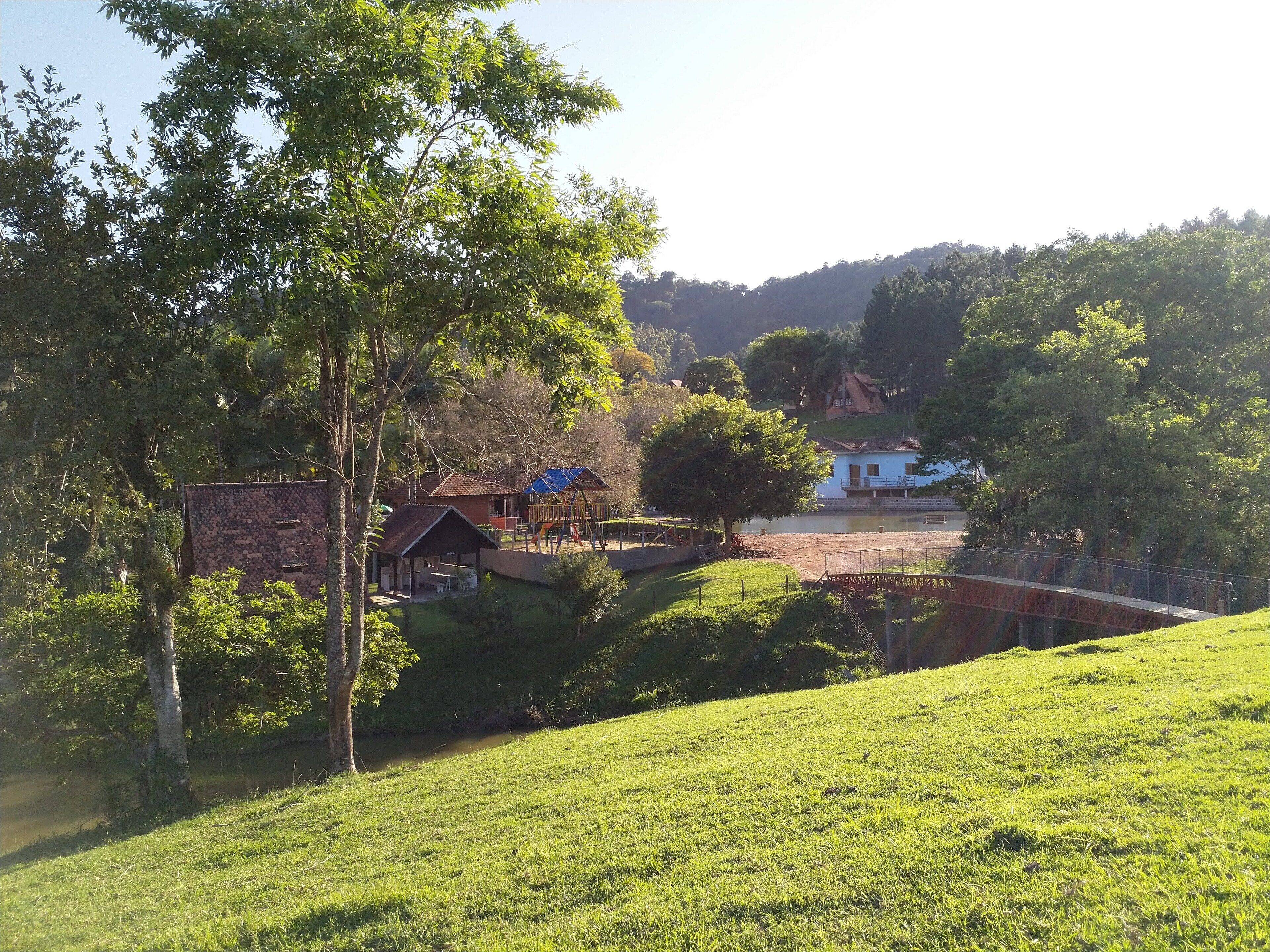 A rural landscape with a grassy hill, a small wooden cabin, and a blue-roofed structure with a playground.
