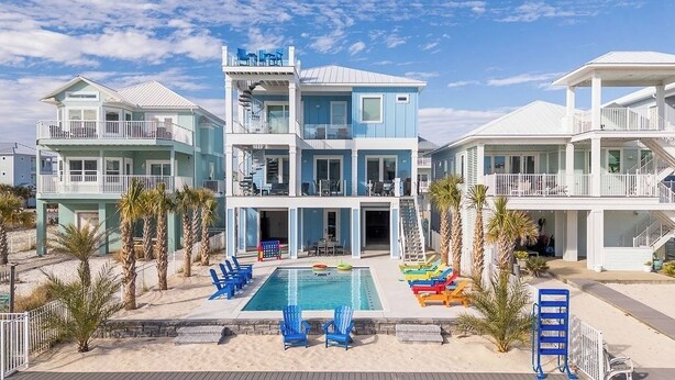 A multi-story beachfront hotel with a swimming pool, outdoor seating, and palm trees. - Here and Now | 🛥️ Canal Access + Pool + Beach Gear + Golf Cart + Sleeps 20 (Navarre)