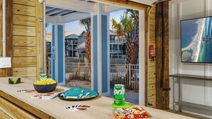 A room with a wooden wall, a TV on the right, a pool table, and a bowl of chips on the left. - Here and Now | 🛥️ Canal Access + Pool + Beach Gear + Golf Cart + Sleeps 20 (Navarre)