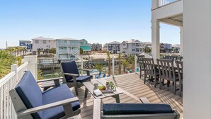 A deck with outdoor seating, overlooking a beach and residential buildings. - Here and Now | 🛥️ Canal Access + Pool + Beach Gear + Golf Cart + Sleeps 20 (Navarre)