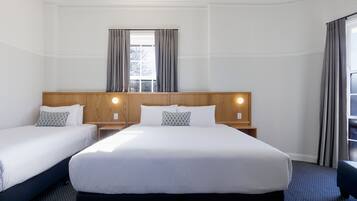A hotel room with two beds, a wooden headboard, a window with curtains, and a nightstand with a lamp.