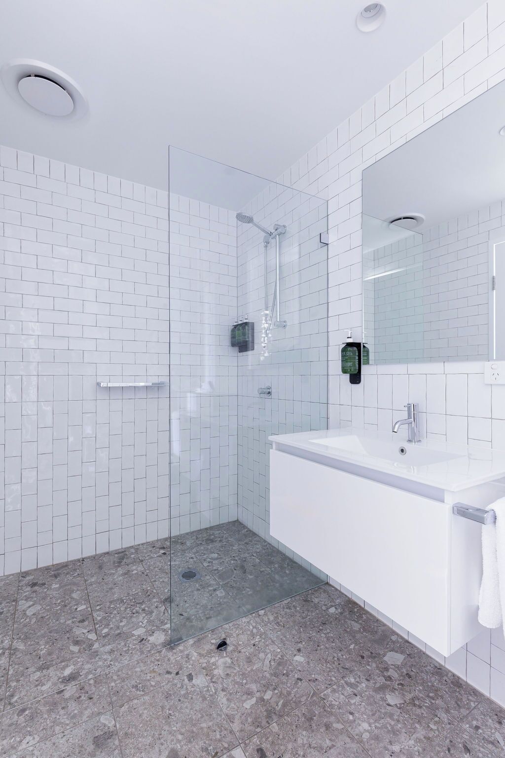 Un baño moderno con azulejos blancos tipo metro, ducha con cerramiento de vidrio, lavamanos blanco y un espejo grande.