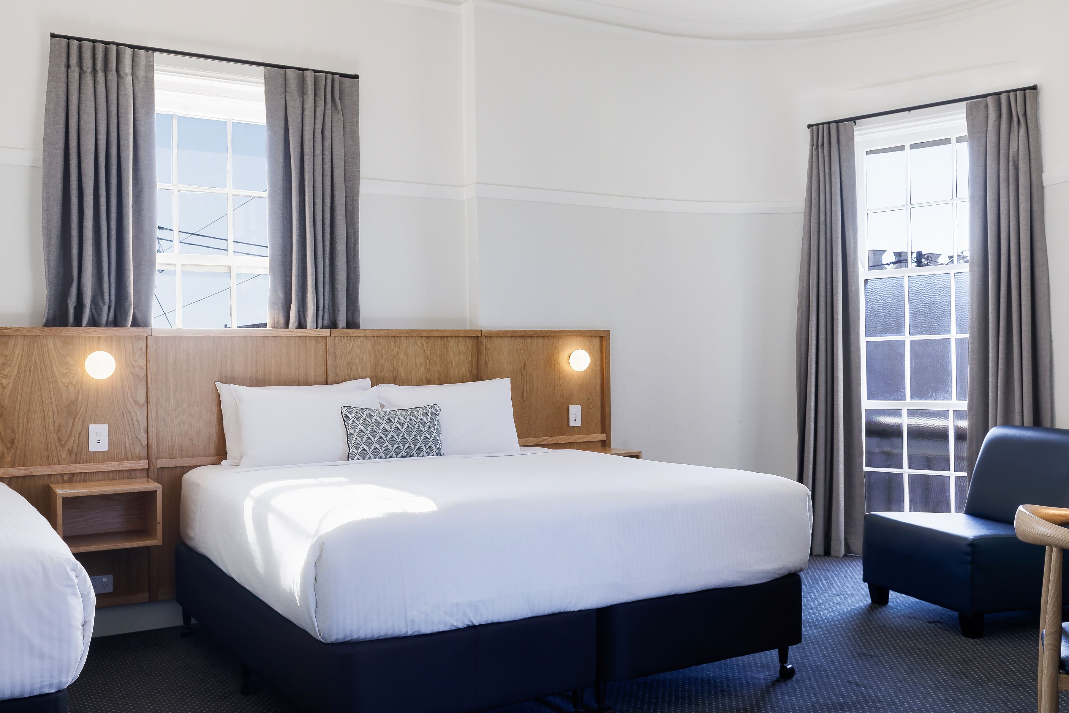 Ett hotellrum med en stor säng, sängbord, en stol och ett fönster med gardiner.