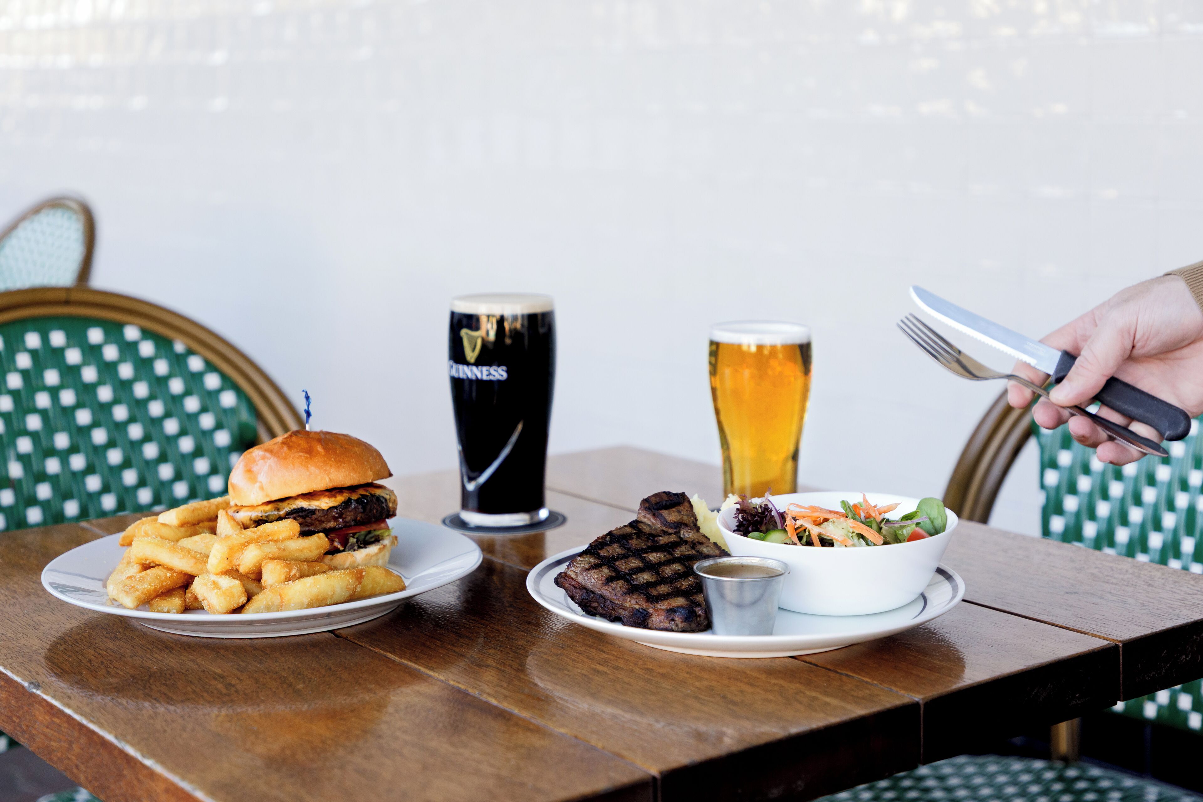Una mesa de comedor con una hamburguesa, papas fritas, un bistec, una ensalada y dos bebidas.