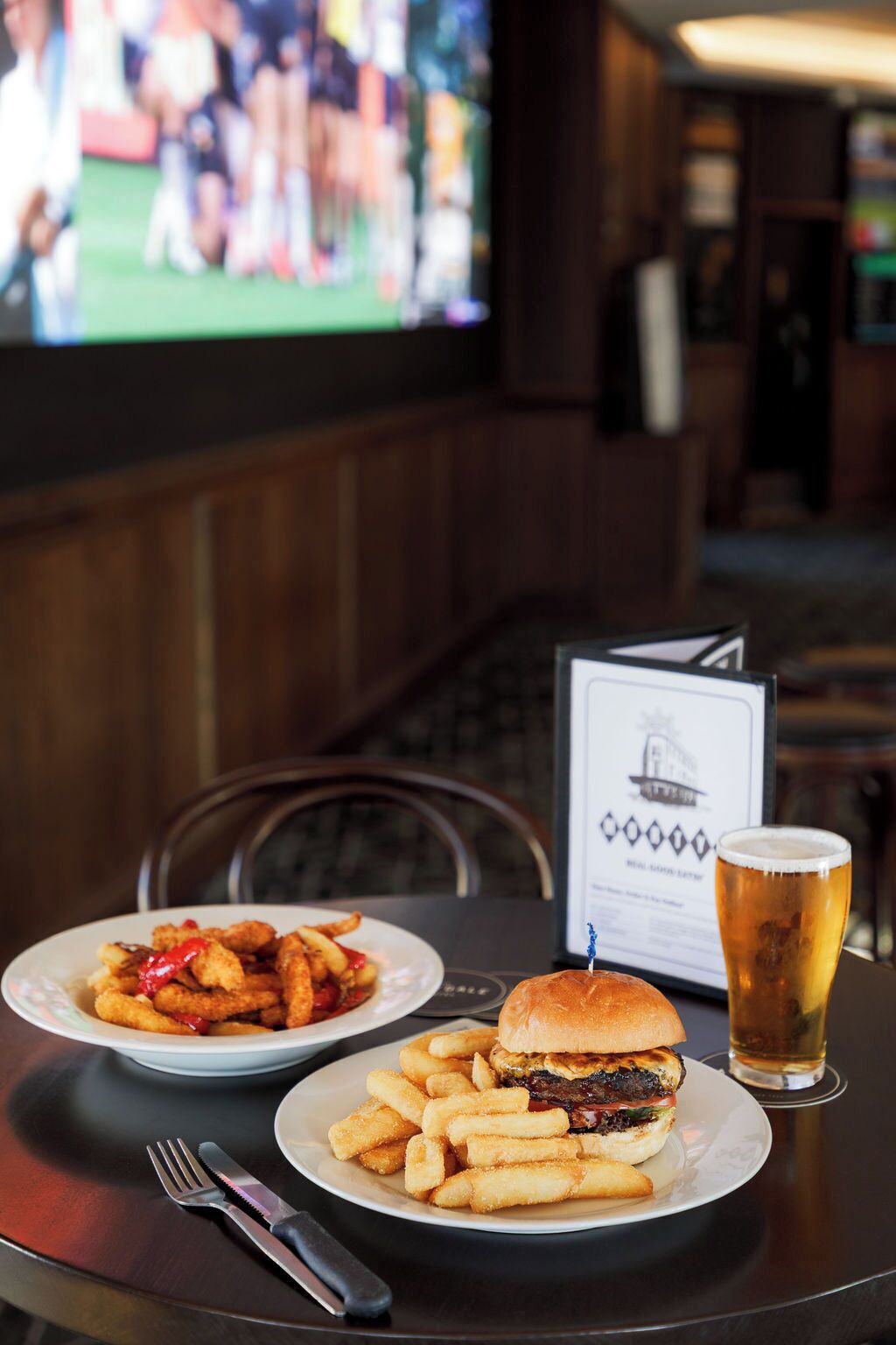 A meal consisting of a burger and fries on a table with a menu and a glass of beer.