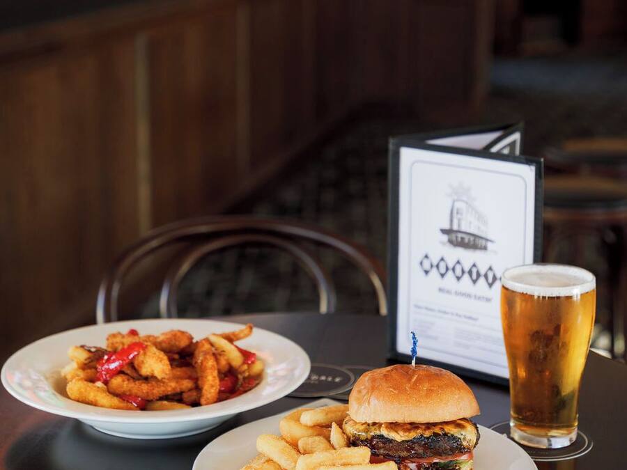 A meal consisting of a burger and fries on a table with a menu and a glass of beer.