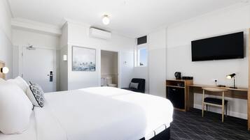 A hotel room with a large bed, a desk, a chair, a flat-screen TV, and a coffee machine.
