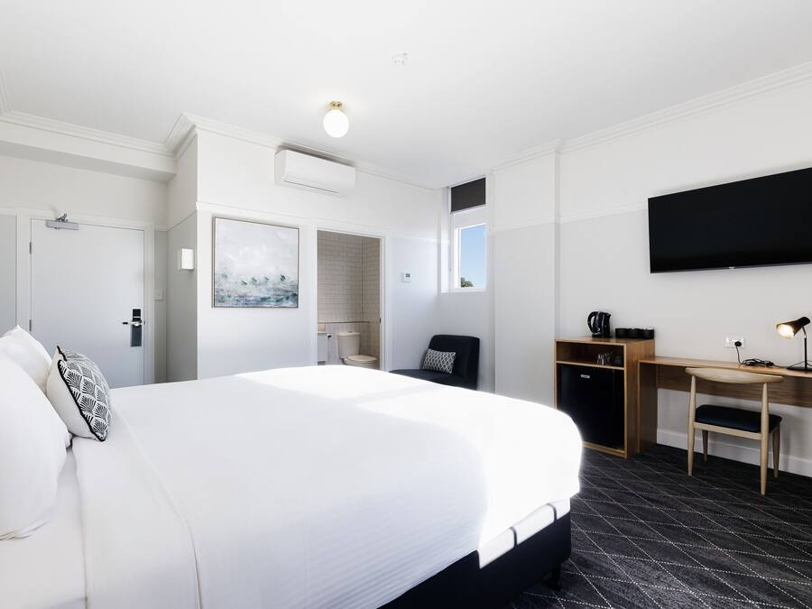 A hotel room with a large bed, a desk, a chair, a flat-screen TV, and a coffee machine.
