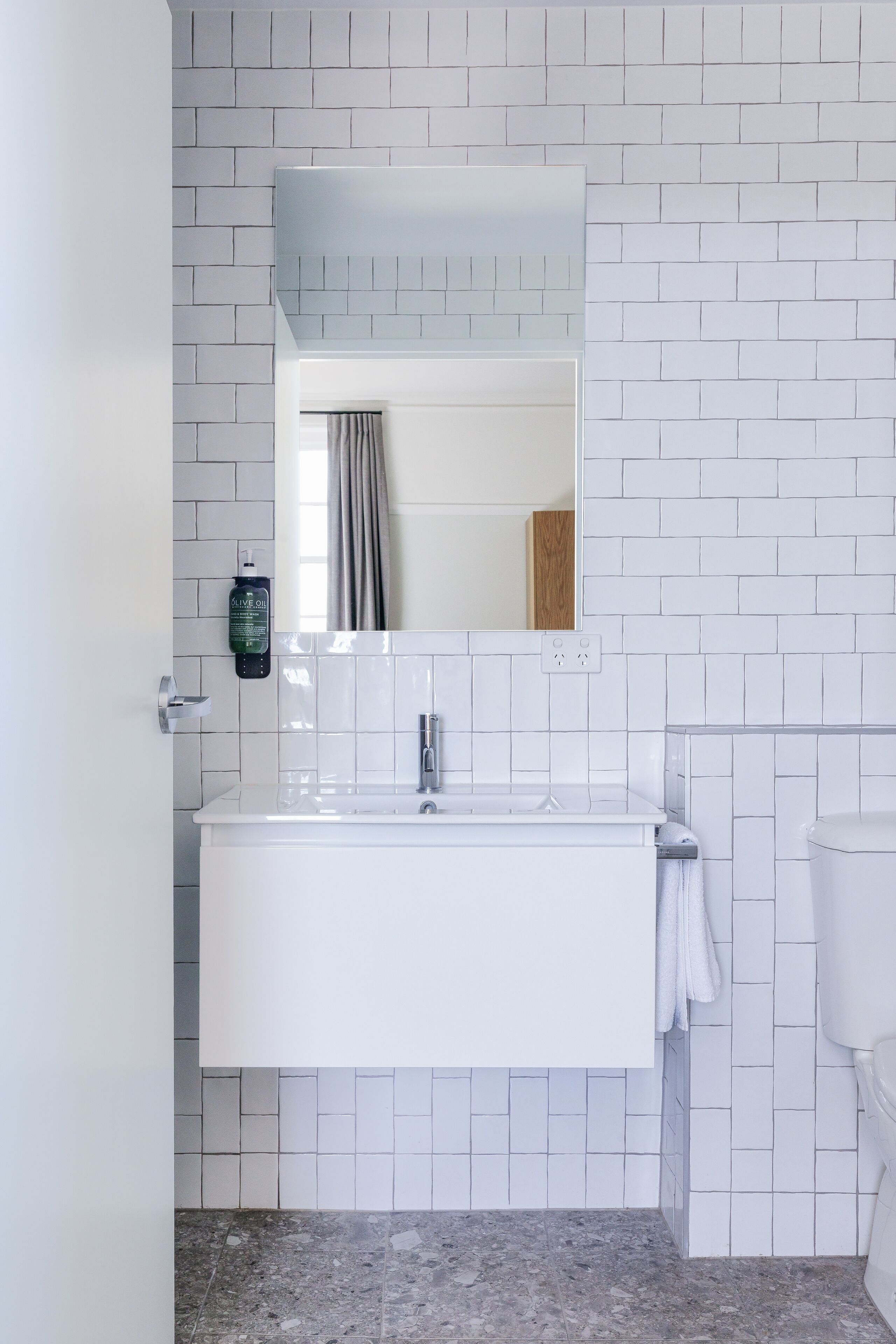 Un baño con lavamanos blanco, espejo y paredes de azulejos.