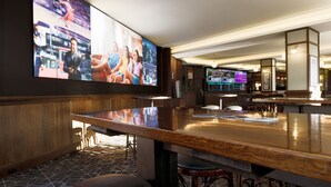 A bar area with a large TV screen displaying sports, a wooden bar counter, and stools. - Mortdale Hotel (Mortdale)