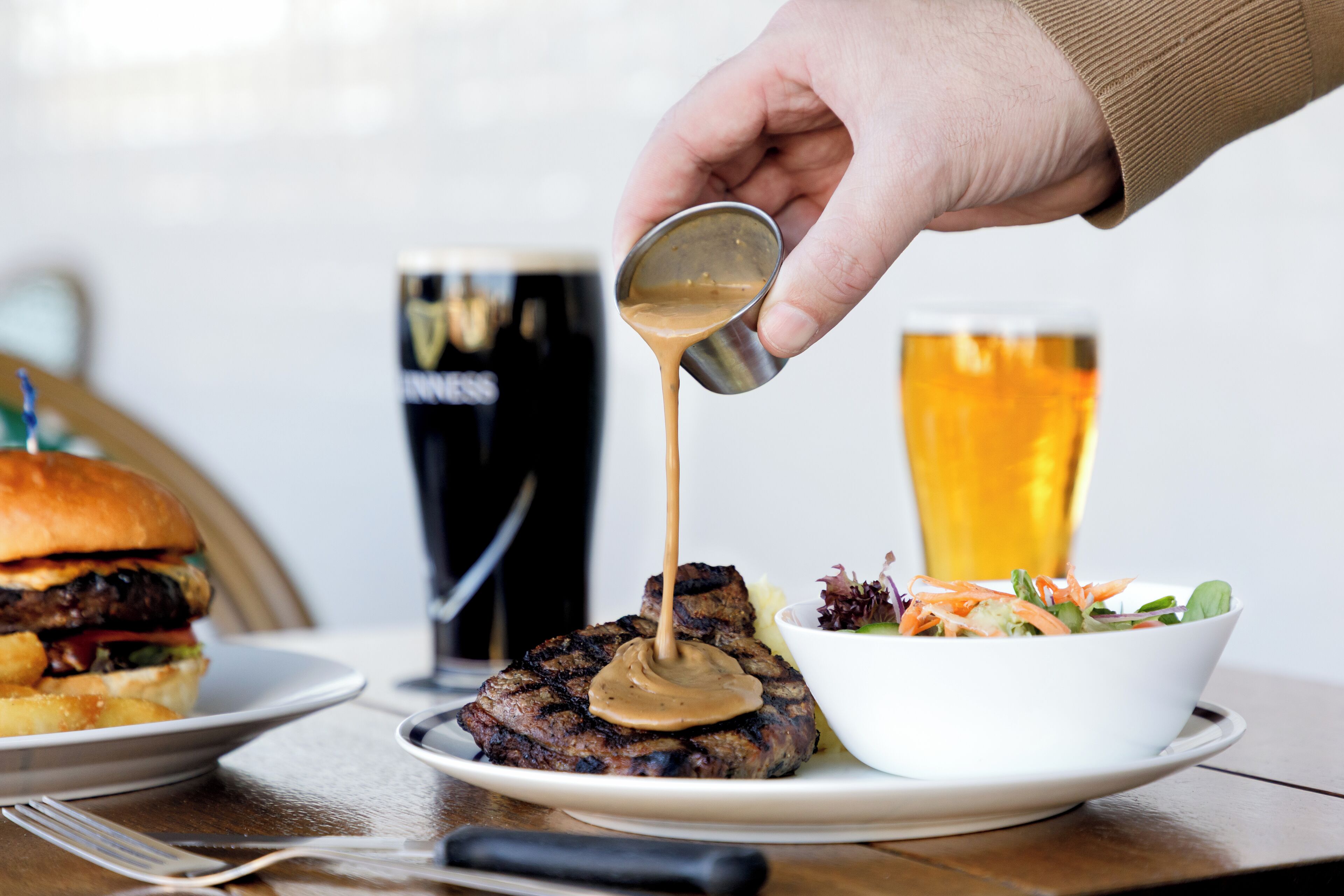 Un steak nappé de sauce, servi dans une assiette, une chope de bière et un saladier rempli de salade.