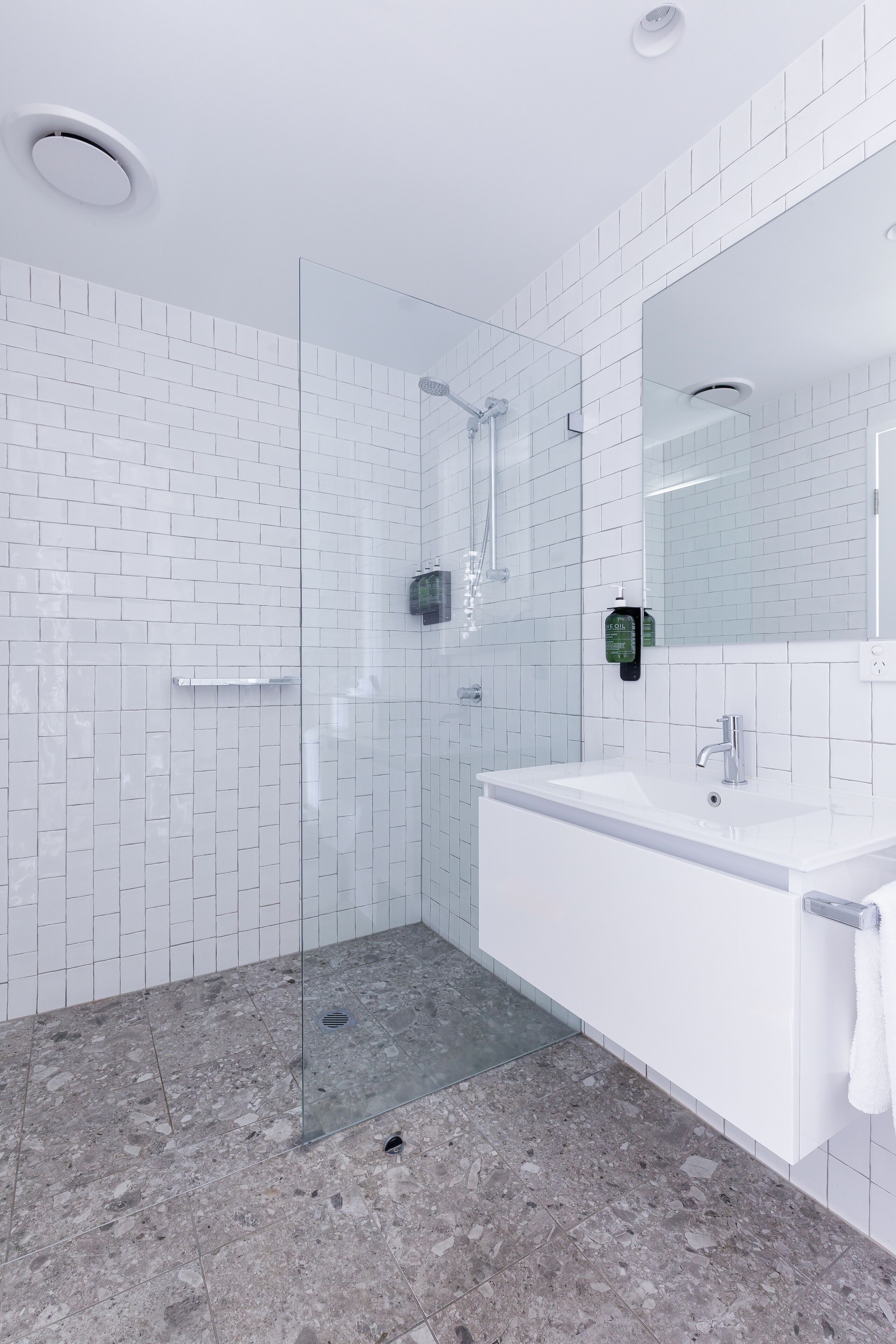 A modern bathroom with white subway tiles, a glass-enclosed shower, a white sink, and a large mirror.