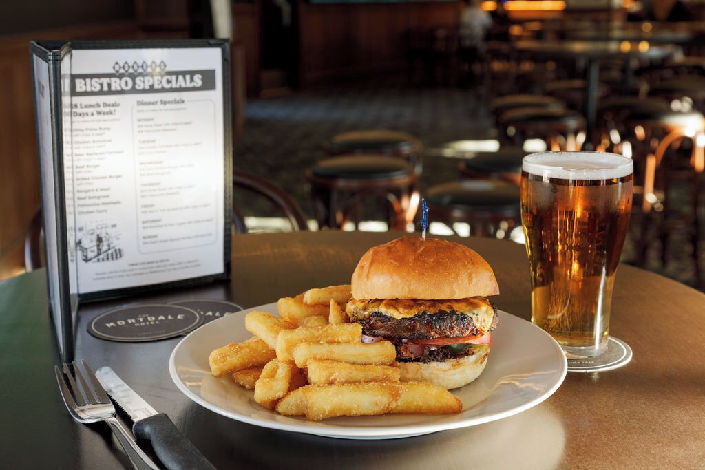 Un panel con el menú que dice 'ESPECIALIDADES DE BISTRO' muestra una hamburguesa con papas fritas sobre una mesa.