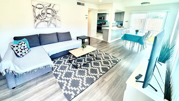 A modern living room with a sofa, coffee table, and artwork. There is a kitchen area with a dining table and chairs. - Luxury home near Disney land. Entire place!
 (Orange)