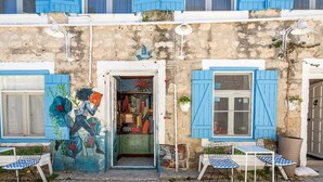 A building with a shop entrance, blue shutters, and outdoor seating.