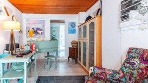 A room with a wooden ceiling, a desk with a lamp, a colorful chair, and a cabinet.