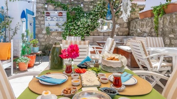 A table set for breakfast with various dishes, including eggs and bread, in an outdoor setting with chairs and potted plants.