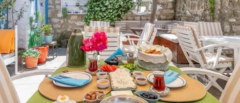 A table set for breakfast with various dishes, including eggs and bread, in an outdoor setting with chairs and potted plants.