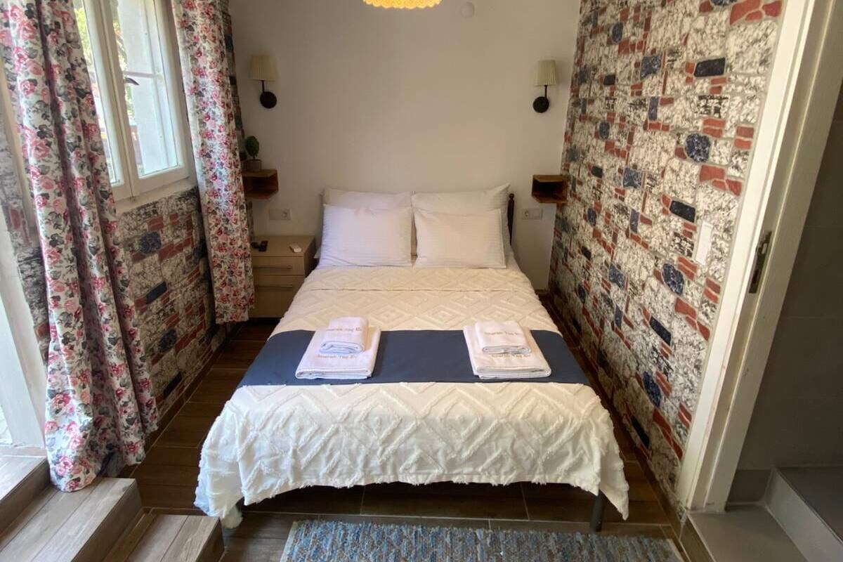 Un dormitorio con cama, cortinas florales, un papel tapiz estampado, un ventilador de techo y una lámpara.