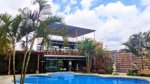 A modern building with a glass facade, a pool, and palm trees. - Gran Hotel Villa Del Sur (San Vicente de Cañete)
